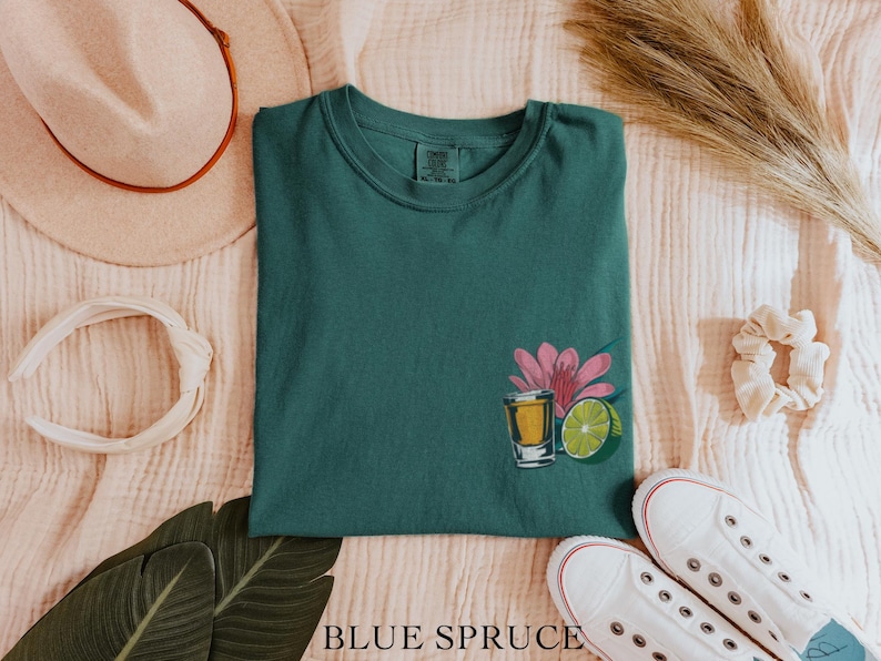 May include: A teal green t-shirt with a graphic of a shot glass of tequila, a lime wedge, and a pink flower.