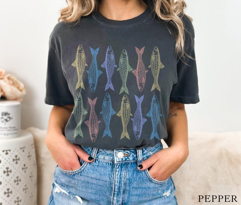 May include: A dark gray t-shirt with a colorful fish pattern. The fish are arranged in rows and are outlined in black. The shirt has a crew neck and short sleeves.