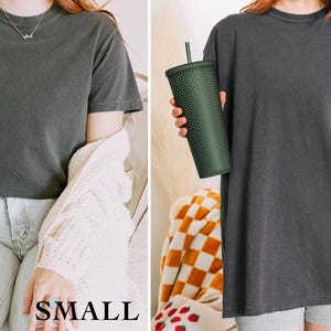 May include: Two women wearing the same charcoal gray t-shirt in different sizes. The woman on the left is wearing a small and the woman on the right is wearing a large. The text "SMALL" and "LARGE" is printed below each woman.