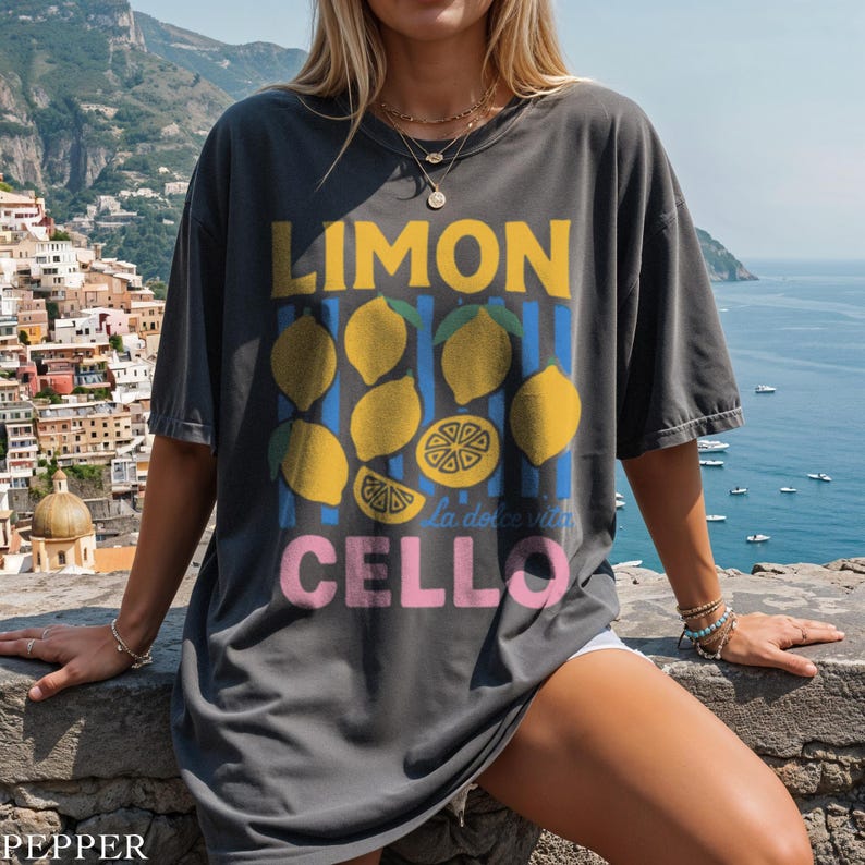 May include: Dark gray t-shirt with a lemon graphic. The design includes the word "LIMON" in yellow, lemons, blue stripes, and the word "CELLO" in pink. The phrase "la dolce vita" is also included.