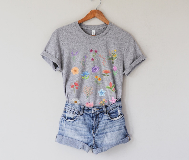 May include: A heather grey t-shirt with a floral print featuring a variety of colorful flowers. The shirt is paired with denim shorts.
