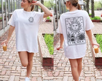 May include: White oversized t-shirt with a black sun graphic on the front and a tarot card design on the back that says "XIX...THE SUN".