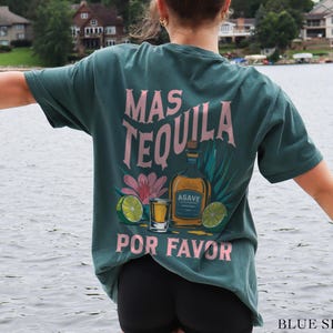 May include: A teal blue t-shirt with a pink graphic that says "Mas Tequila Por Favor" and features a bottle of tequila, a shot glass, and limes.