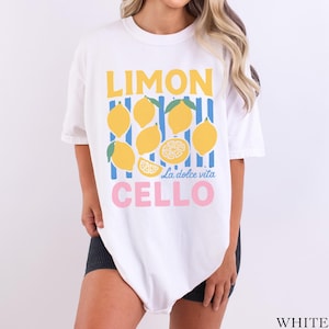 May include: White t-shirt with a lemon-themed graphic. The design features yellow lemons, blue and yellow stripes, and the words "LIMON CELLO" in yellow and pink, with "La dolce vita" in the middle.