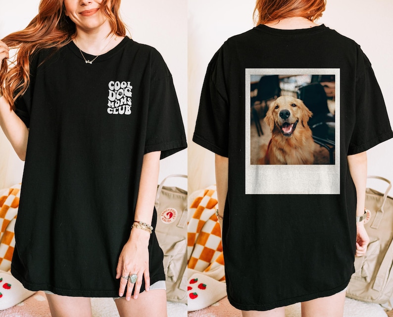 May include: Black t-shirt with the text "Cool Dog Moms Club" printed on the front. The back of the shirt features a photo of a golden retriever dog in a Polaroid frame.
