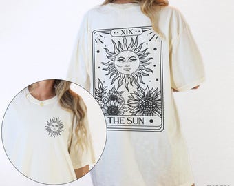 May include: A white oversized t-shirt with a black and white graphic of a tarot card depicting the sun. The text "XIX THE SUN" is printed on the card. The shirt is available in ivory.