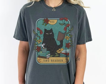 May include: A dark grey t-shirt with a vintage tarot card design featuring a black cat reading a book. The card is labelled "VII THE READER" and has floral accents.