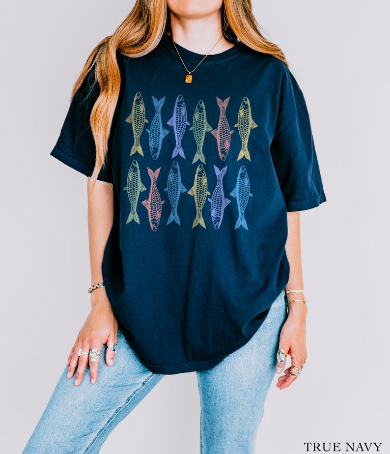 May include: A navy blue t-shirt with a colorful fish pattern. The fish are outlined in different shades of blue, green, yellow, and pink. The shirt has a relaxed fit and a crew neck.