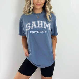 Puede incluir: Una camiseta azul con texto blanco que dice "SAHM UNIVERSITY".