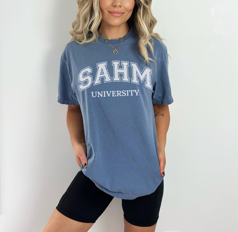 Puede incluir: Una camiseta azul con texto blanco que dice "SAHM UNIVERSITY".