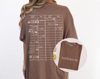 May include: A brown t-shirt with a white graphic of a library card with dates and the text "bookworm" printed on the front.