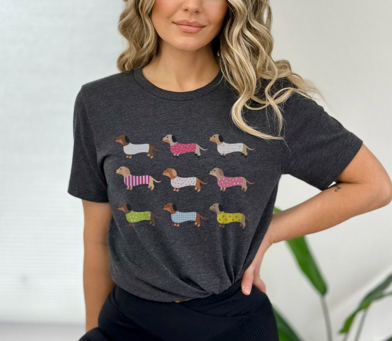May include: A dark gray t-shirt with a graphic print of nine dachshunds wearing different patterned pajamas. The dachshunds are all facing the right side of the image.