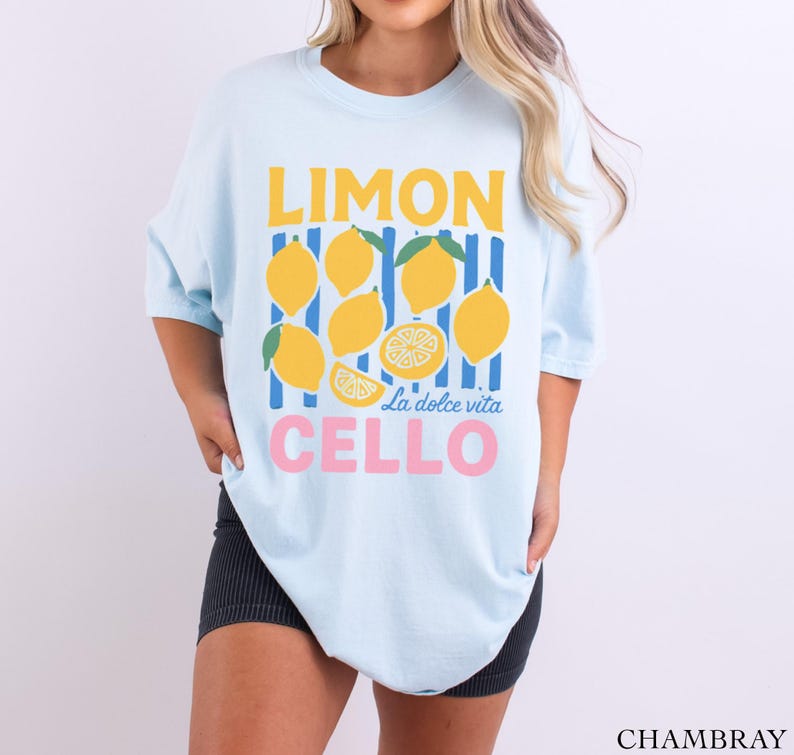 May include: Light blue t-shirt with a lemon-themed graphic. The design features yellow lemons, blue and yellow stripes, and the words "LIMON CELLO" in yellow and pink, with "La dolce vita" in the middle.