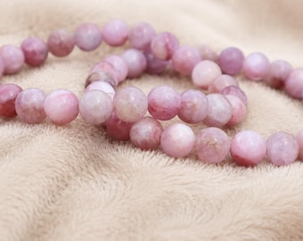 May include: A beaded bracelet featuring round, polished pink gemstone beads with a silver-toned metal charm shaped like a ship's wheel. The text Shriyeegems is visible in the upper right corner of the image.