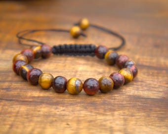 May include: A beaded bracelet featuring polished tiger eye stones in shades of brown, gold, and red. The bracelet is strung on a black cord with an adjustable closure. The beads are approximately 0.4 inches in diameter.