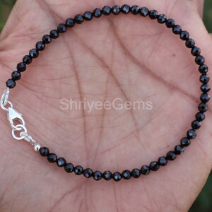 May include: A black diamond bracelet with a silver clasp. The bracelet is made of small, faceted black diamonds and is approximately 18 cm in length.