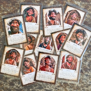 May include: A collection of trading cards featuring illustrated portraits of biblical figures. Each card has a portrait, name, and text. The cards are in clear plastic sleeves. The cards are on a wooden surface.