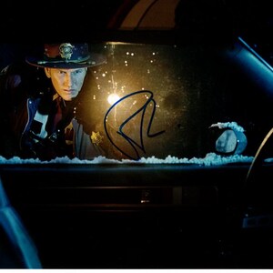 May include: A man wearing a brown and gold police hat is looking out of a car window. The car is covered in snow and the man's signature is visible on the window.