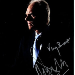 May include: A black and white photo of a man in a suit and tie. He is looking to the side and has a serious expression on his face. The photo is signed "Very Best" and "Nash" in silver ink.