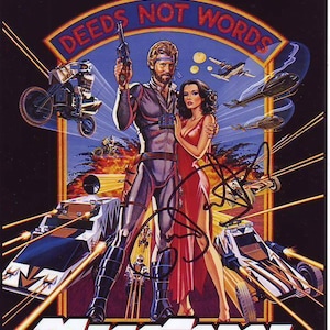 Peut inclure: Une affiche de film pour le film "Megaforce" mettant en scène un homme et une femme en tenue futuriste debout devant un véhicule futuriste. L'affiche porte le texte "Deeds Not Words" dans un grand cercle en haut.