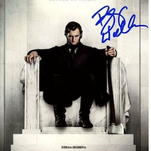 Könnte beinhalten: Ein Filmplakat für den Film "Abraham Lincoln: Vampire Hunter". Das Plakat zeigt ein Schwarzweißbild eines Mannes, der auf einem Thron sitzt und eine Axt hält. Der Text "Präsident bei Tag, Jäger bei Nacht." befindet sich oben auf dem Plakat. Der Titel des Films befindet sich unten auf dem Plakat.