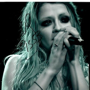 May include: A woman with long blonde hair sings into a microphone. She is wearing a black tank top and has a microphone in her hand.