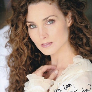 Puede incluir: Una mujer con el pelo largo y rizado castaño lleva una blusa blanca con cuello de volantes. Está mirando a la cámara y sonriendo. El texto "my love!" y una firma están escritos en tinta negra en la blusa.