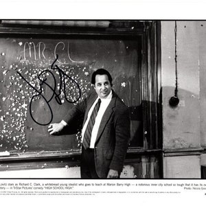 May include: Black and white photo of a man standing in front of a chalkboard. The chalkboard has the words "Mr. C" written on it. The man is wearing a suit and tie. He is looking at the camera. The photo is from the movie "High School High".