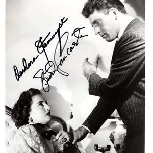 Puede incluir: Fotografía en blanco y negro de dos personas, un hombre y una mujer, en una pose dramática. La mujer está sentada, sosteniendo un teléfono, mientras el hombre se inclina. La imagen está firmada por Barbara Stanwyck y Joan Castle.