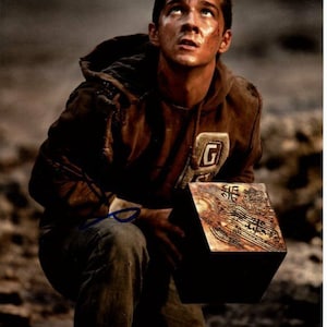 May include: A distressed brown hoodie with a large "G" patch is worn by a person looking upward. The person is holding a detailed, ornate, dark-colored cube. The image has a cinematic, dramatic feel.