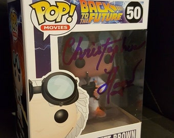 May include: A white cardboard box with a clear plastic window showing a Pop! Movies vinyl figure of Dr. Emmett Brown from Back to the Future. The figure is holding a device and has a white lab coat and goggles. The box has the words "Pop! Movies" and "Back to the Future" on it, along with the number "50". The box also has a warning label that says "Choking Hazard" and "May contain small parts".