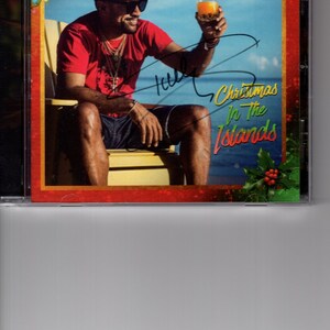 Puede incluir: Una portada de CD con el artista de reggae Shaggy, que lleva un sombrero de paja y gafas de sol, sosteniendo un vaso de zumo de naranja. La portada se titula "Christmas In The Islands" con la firma de Shaggy.