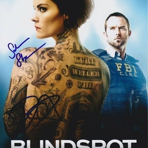 Puede incluir: Un póster para la serie de televisión "Blindspot" con una mujer con un tatuaje en toda la espalda y un hombre con un chaleco del FBI. El tatuaje de la mujer incluye las palabras "Kurt Weller" y "FBI".
