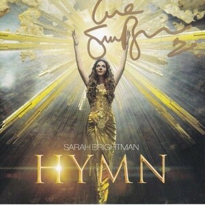 Puede incluir: Una mujer con un vestido dorado con los brazos en alto, de pie frente a un fondo amarillo y blanco brillante. El texto "HYMN" está en letras grandes y negritas debajo de ella. El texto "SARAH BRIGHTMAN" está en letras más pequeñas encima de la palabra "HYMN".