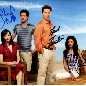 May include: Four people are standing in front of a blue sky and a wooden fence. The people are all smiling and looking at the camera. The person on the left is wearing a red dress. The person in the middle is wearing a blue and white striped shirt. The person on the right is wearing a white shirt and a blue tie. The person in the back is wearing a blue shirt. The people are all holding autographed photos of themselves.