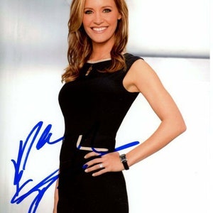 May include: A woman with long brown hair is wearing a black sleeveless dress. She is smiling and has her hand on her hip. She is wearing a watch on her left wrist and a ring on her right hand.