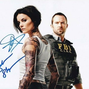 Puede incluir: Una fotografía firmada de dos actores, una mujer con el pelo negro corto y tatuajes en los brazos, y un hombre con el pelo castaño corto que lleva un chaleco negro con las letras "FBI C.I.R.G." impresas.