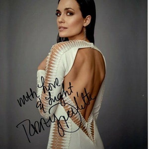 Può includere: Una donna in un abito bianco con la schiena in pizzo posa per una foto. Indossa un paio di orecchini e ha i capelli tirati indietro. La foto è firmata "con amore e luce,  [signature]"