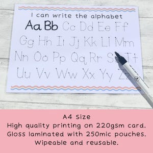 May include: A white laminated A4-sized card with dotted lines for tracing the alphabet. The card has a pink and blue wavy border. The text "I can write the alphabet" is at the top of the card. A black dry-erase marker is lying on the card.
