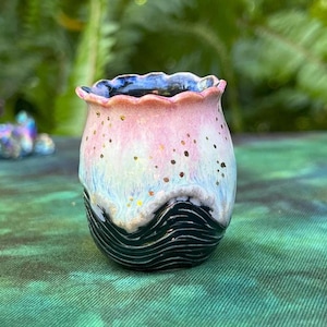 May include: A small, pink and black ceramic planter with a wavy design. The planter has a speckled glaze and a black rim.