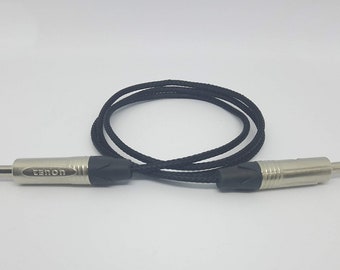 May include: A black audio cable with two silver-colored 1/4 inch (6.35 mm) TS connectors. The cable is coiled in a loop. The connectors have black rubber strain reliefs.