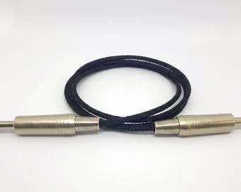 May include: A black braided audio cable featuring two silver-toned metal 1/4-inch TRS jack connectors at each end. The cable is coiled into a circular shape, showcasing the textured fabric exterior of the cord and the metallic finish of the plugs.