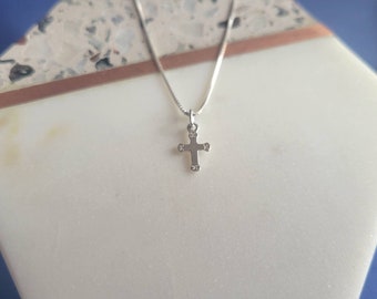 May include: A silver chain necklace with a small silver cross pendant. The cross has four small, clear stones on each point.