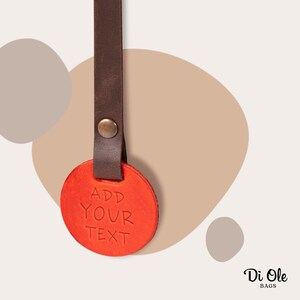May include: A red leather keychain with a brown leather strap. The keychain has the text "ADD YOUR TEXT" embossed on it.