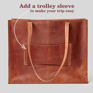 May include: A brown leather tote bag with a front pocket and two long handles. The bag has a trolley sleeve. Text on the image says "Add a trolley sleeve to make your trip easy."