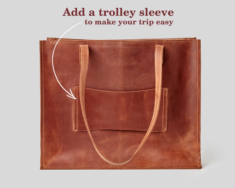 May include: A brown leather tote bag with a front pocket and two long handles. The bag has a trolley sleeve. Text on the image says "Add a trolley sleeve to make your trip easy."