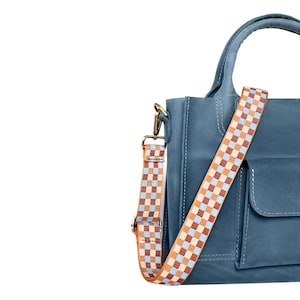 May include: A blue leather handbag with a checkered strap. The bag has a flap pocket on the front and a top handle.