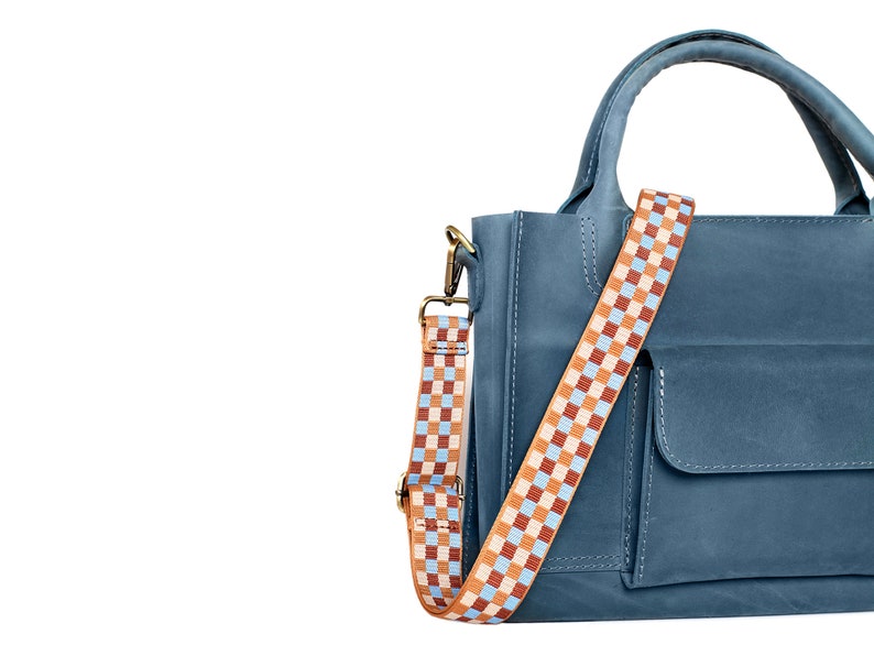 May include: A blue leather handbag with a checkered strap. The bag has a flap pocket on the front and a top handle.