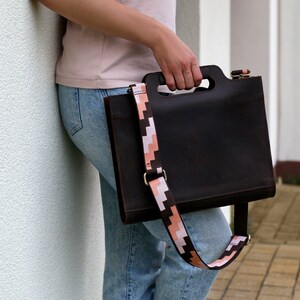 Puede incluir: Un bolso tote de cuero marr&oacute;n con una correa de patr&oacute;n geom&eacute;trico. El bolso tiene un asa superior y una correa para el hombro.