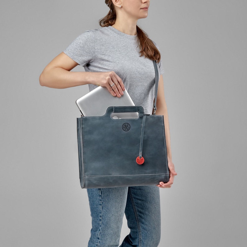 The woman puts her laptop in a gray leather bag with initials engraved on the front. Custom bag for 15 macbook. Gift for her.